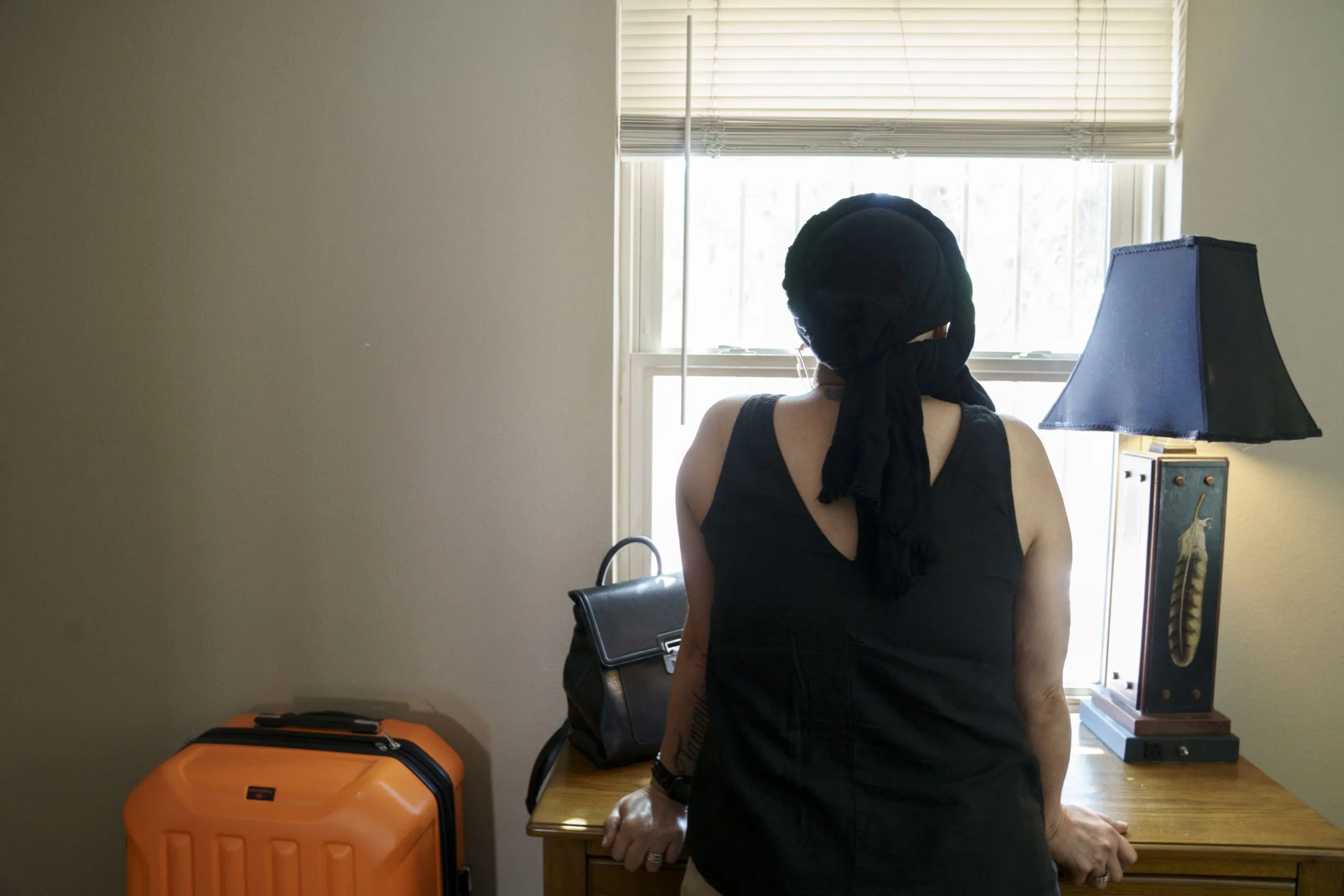 Angelica, a cancer patient who could not find care in her hometown of Las Cruces, looks out the window of the Albuquerque apartment where she’s living while receiving treatment. Nadav Soroker/Searchlight New Mexico